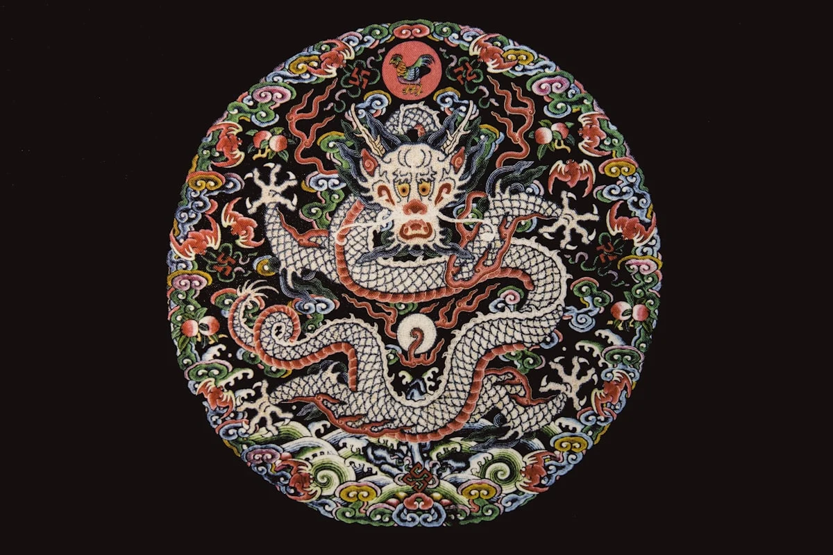 Chinesische Kaiserstickerei: Lóng-Drache auf schwarzem Seidenmedaillon, umgeben von Wolken und Wasser — Symbol für Weisheit, Himmel und kosmische Ordnung