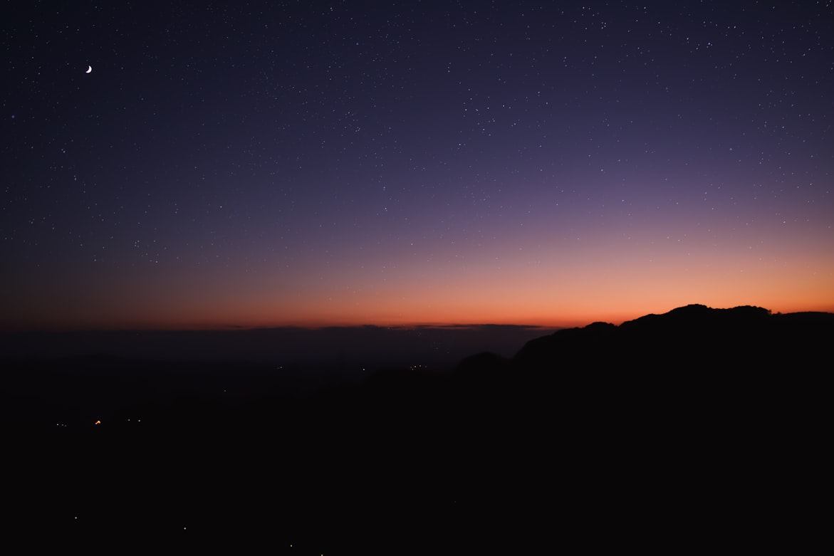 Dämmerungshimmel mit Mondsichel und Sternen über einer Bergsilhouette