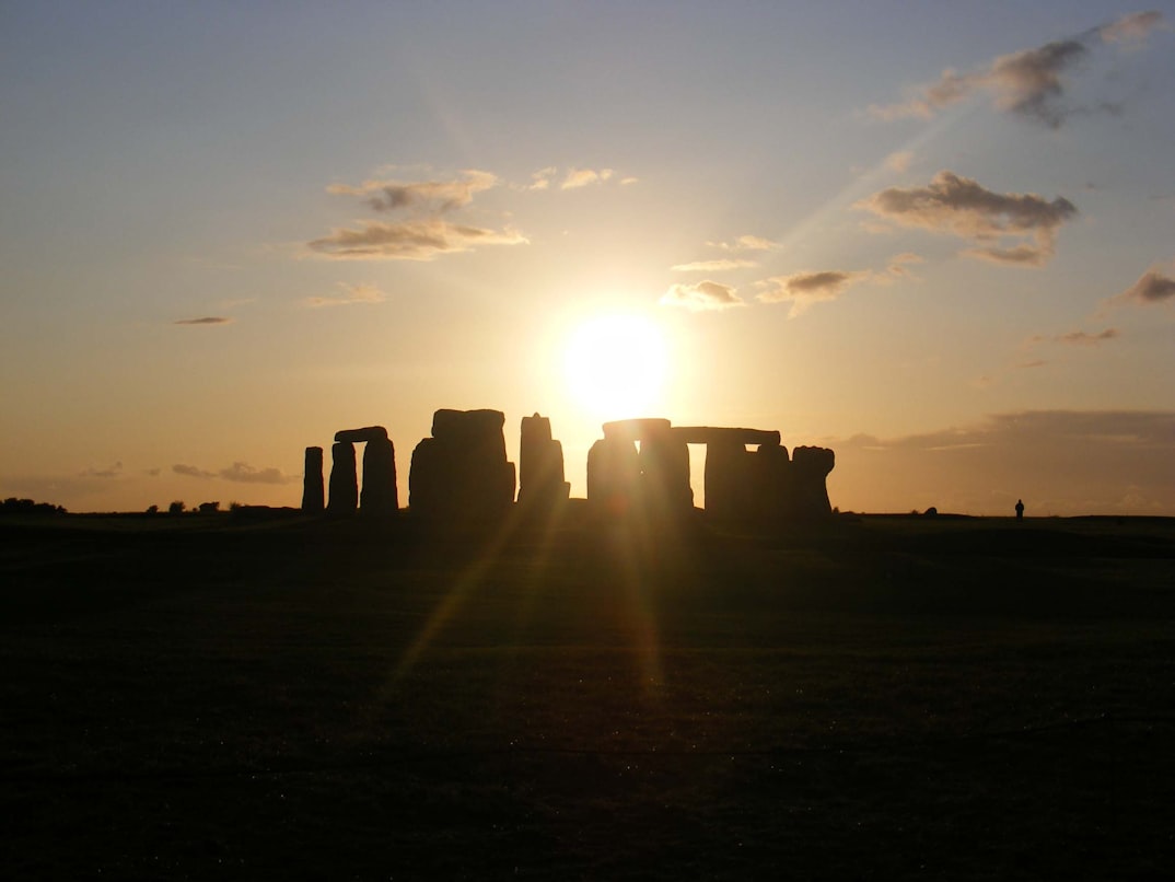 Stonehenge als Silhouette gegen die untergehende Sonne — die Steine werfen lange Schatten über die Salisbury Plain